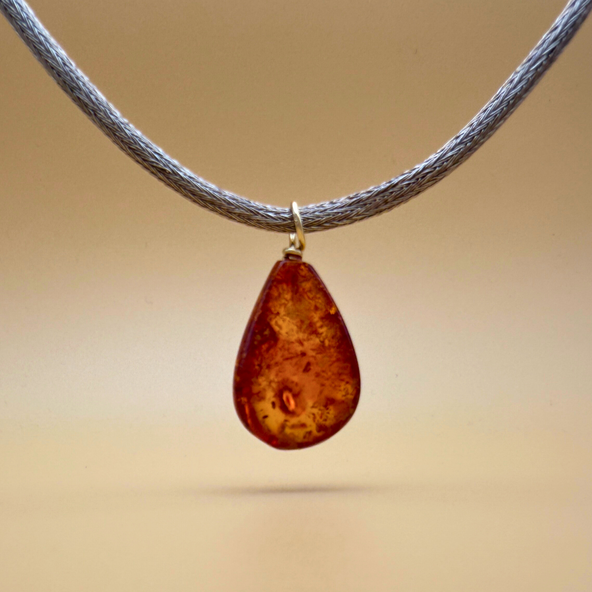 Backside of Teardrop-shaped amber pendant with gold on a handknitted chain - Ravgaard