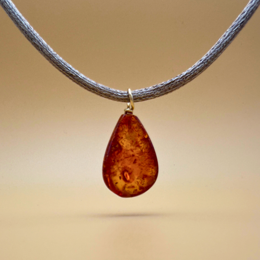 Backside of Teardrop-shaped amber pendant with gold on a handknitted chain - Ravgaard